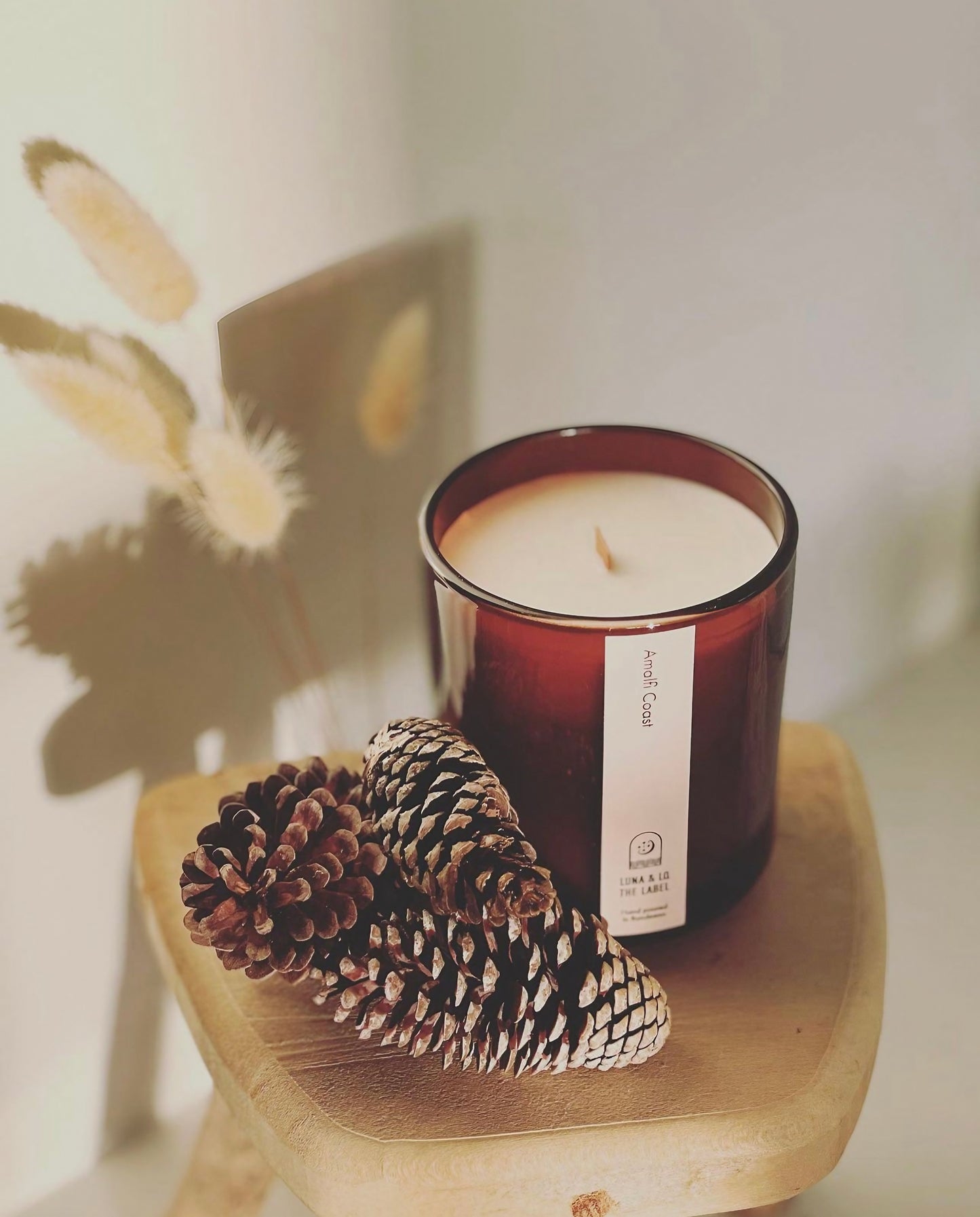 Amalfi Coast Candle by Luna & Lo displayed on a wooden stand with pine cones
