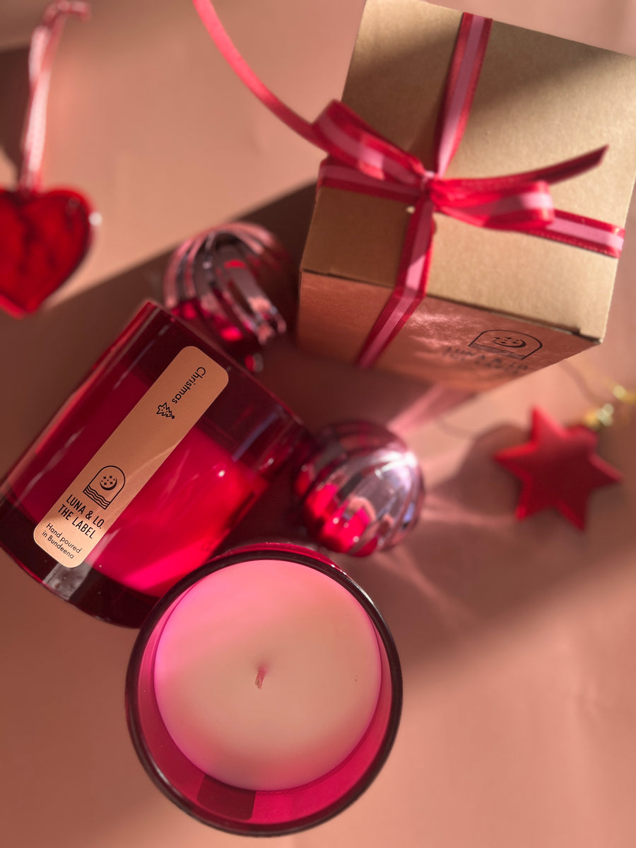 Candle in a red container with a bow and decorative elements on a light background
