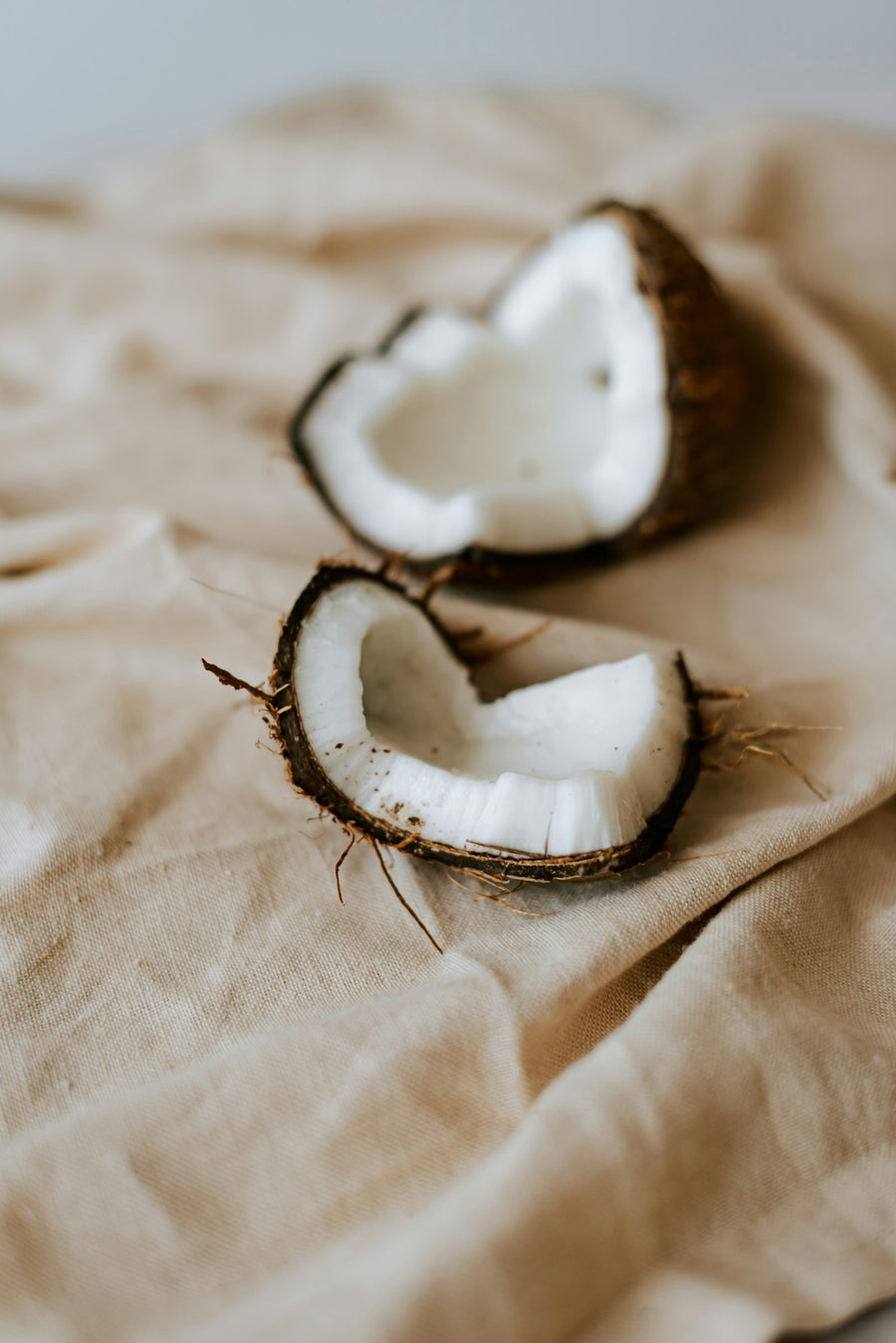Cracked coconut halves resting on soft sand-coloured linen, for Luna & Lo. warm and sweet candles